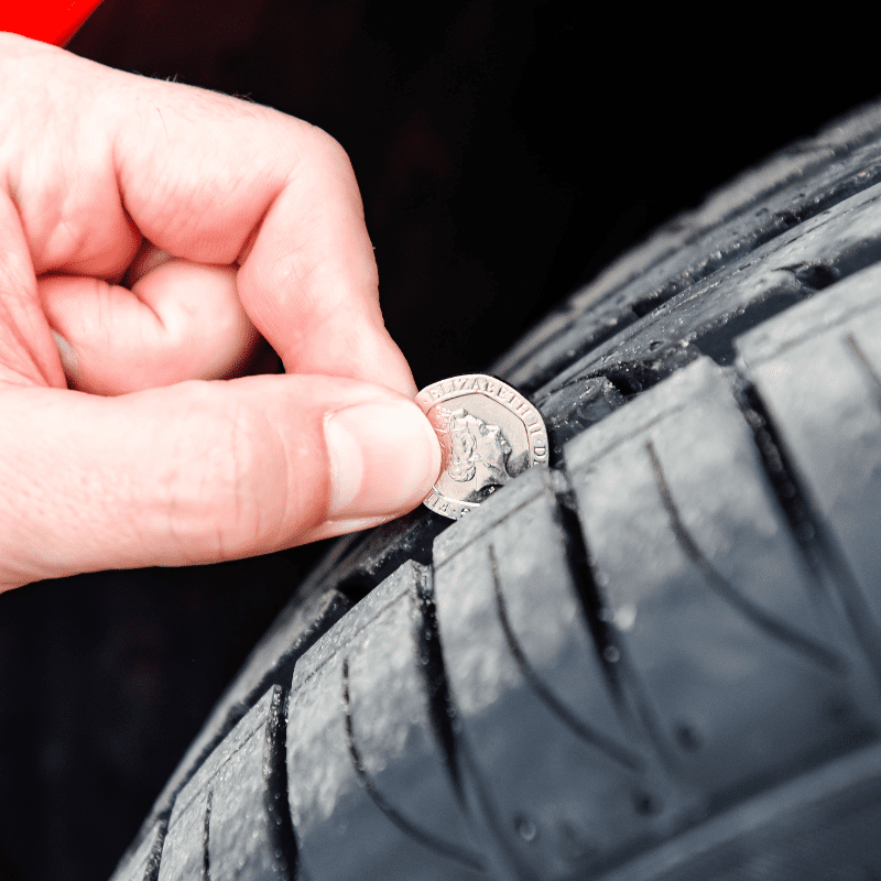 A person inserting a coin on a car tire’s tracks.